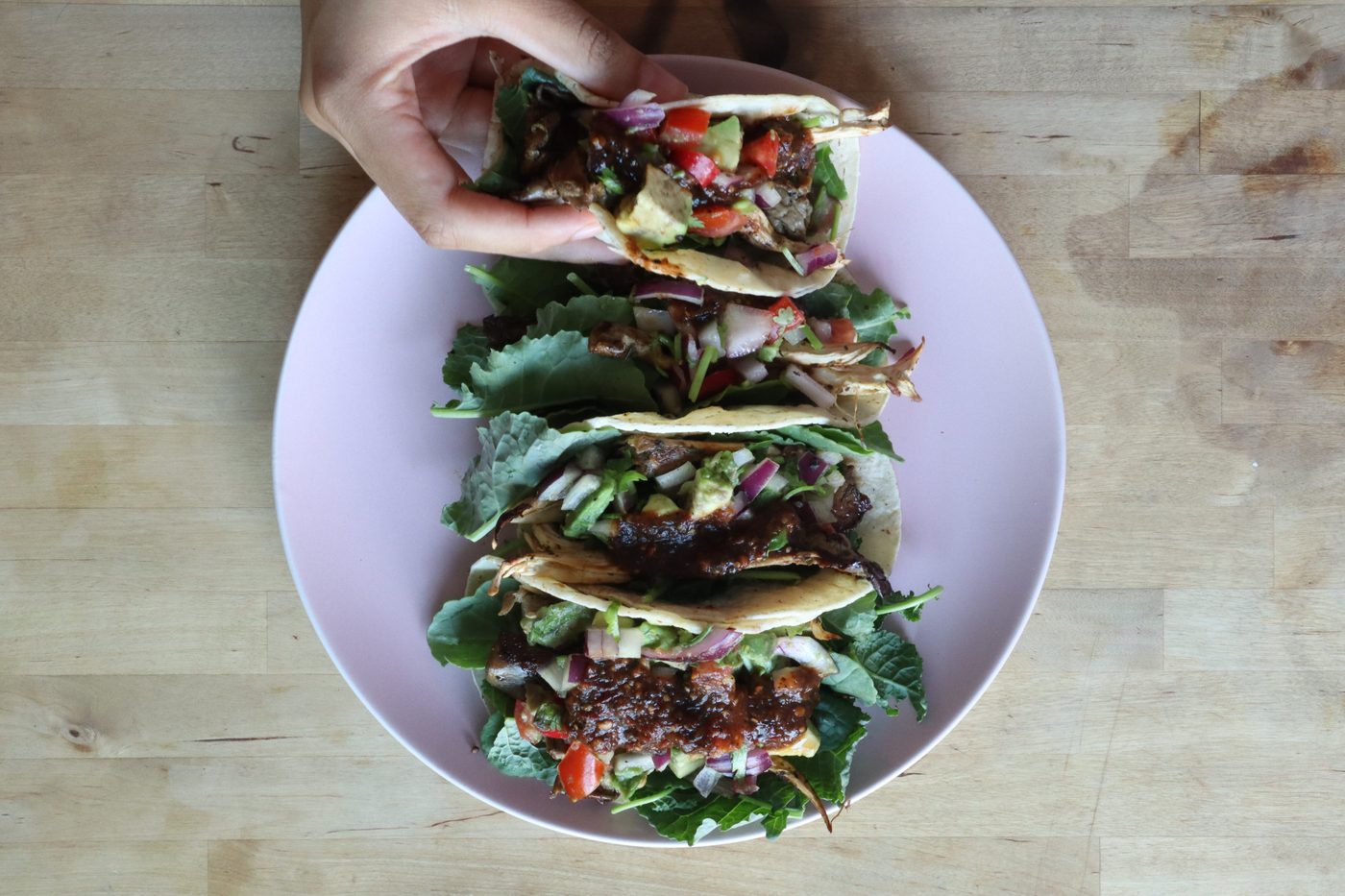 Overhead shot of four tacos with mushroom, salsa, avocado, and kale on a pink plate