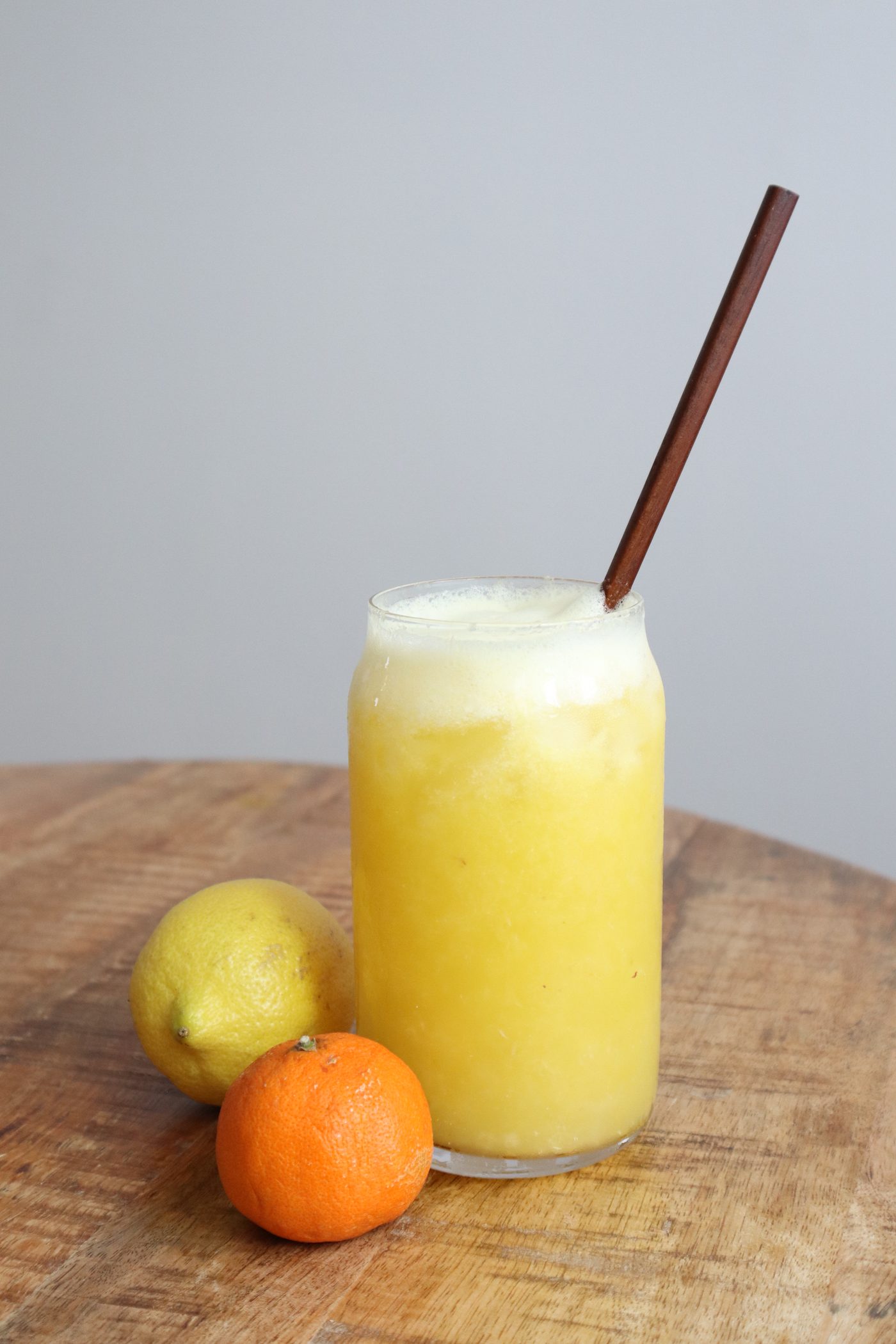 Citrus smoothie glass on a wood table against a grey backdrop, lemon and tangerine beside it