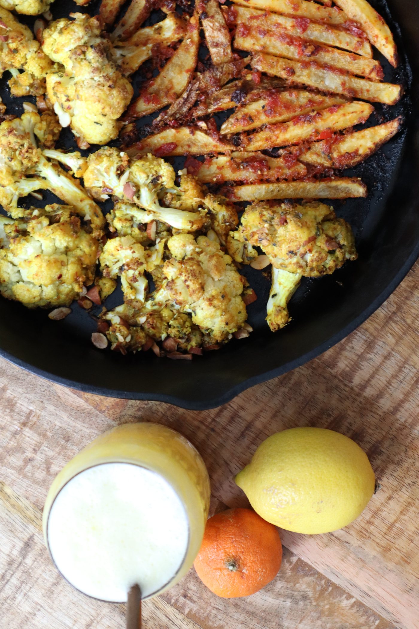Close crop of roasted cauliflower and fries in a skillet with lemon, tangerine, and citrus juice